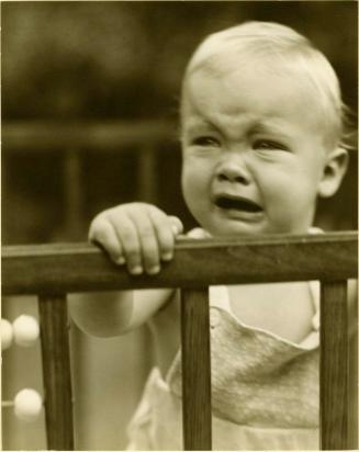 Portrait of crying baby standing up in a playpen
