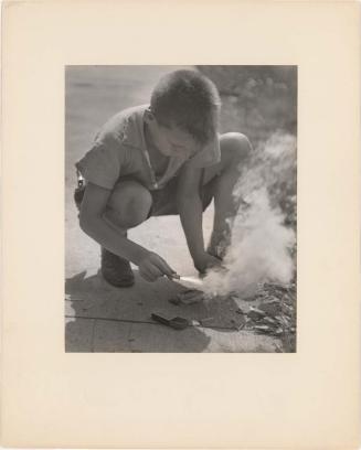 Boy lighting firecrackers on sidewalk